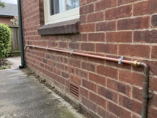 Copper water pipe repaired along a brick exterior wall beside a window in Concord