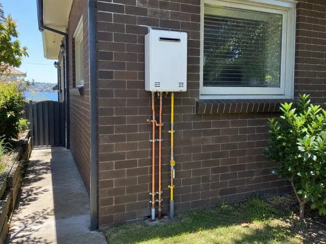 Outdoor wall-mounted hot water unit with copper and gas pipes on a brick house wall in Mortlake